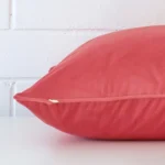 Coral cushion laid horizontally. This perspective shows the edge of the velvet fabric and its square shape.