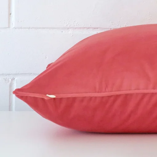 Coral cushion laid horizontally. This perspective shows the edge of the velvet fabric and its square shape.