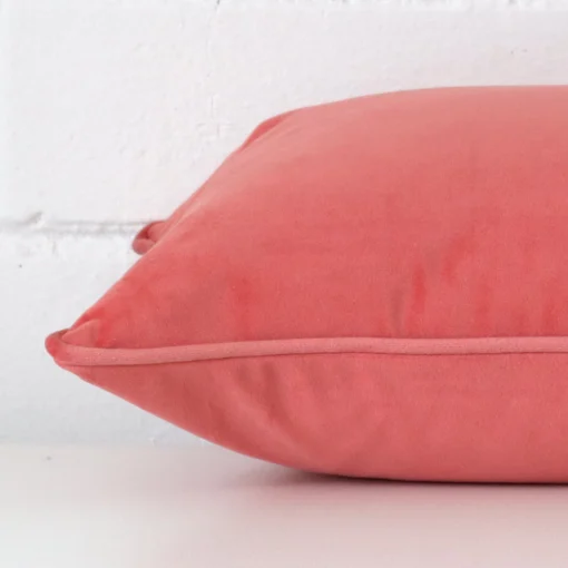 The edge of this velvet square cushion in coral is shown. The shot shows the front and rear panels.