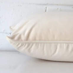 A side view of cream cushion that has velvet fabric and a rectangle size.
