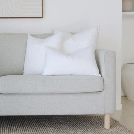 A set of 3 indoor faux feather cushion inserts positioned on the end of a couch.