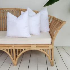 A set of 3 faux feather outdoor cushion inserts positioned on the end of a sofa.