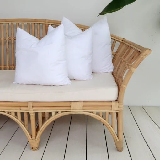 A set of 3 faux feather outdoor cushion inserts positioned on the end of a sofa.