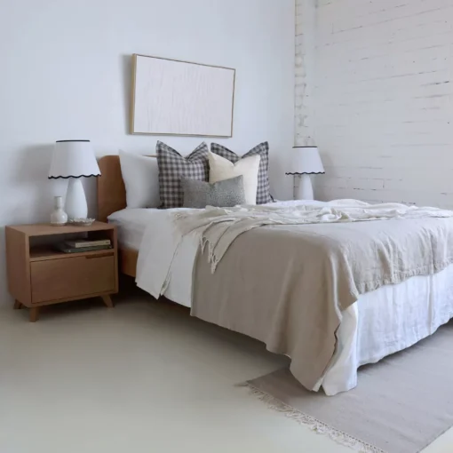 A bright, airy white bedroom with four bed designer cushions resting on a wooden bed.