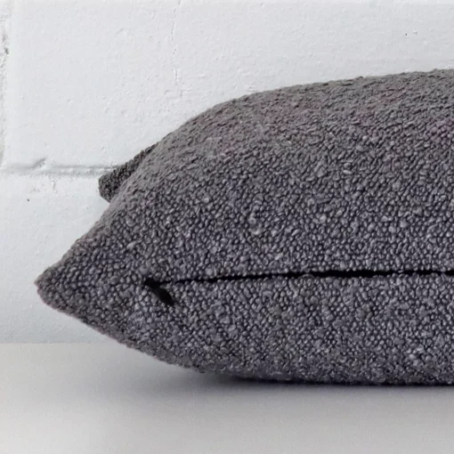 A sideways perspective of this boucle cushion. The positioning shows the border of the rectangle shape and the grey colour.