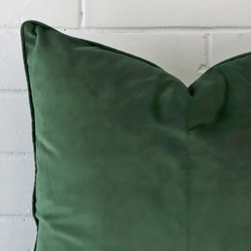 Close up view showing a corner of this velvet cushion in a square size and with dark sage colouring.