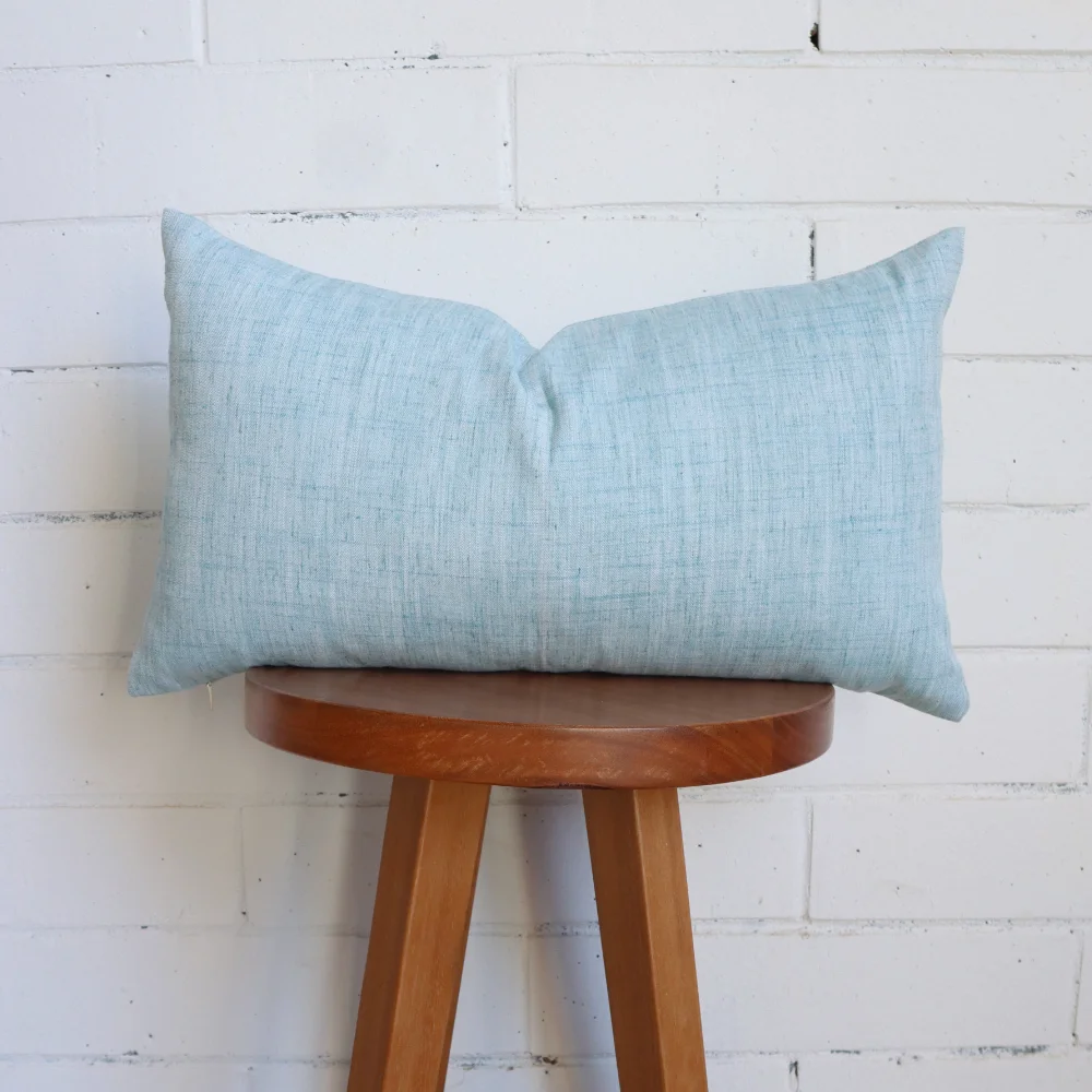 A duck egg blue cushion is positioned on top of a wooden stool.