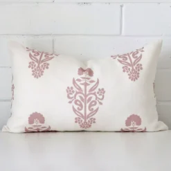 White wall with a floral light pink cushion laying against it. It has a distinctive linen fabric and has a rectangle shape.