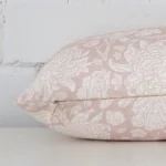 A sideways perspective of this floral linen cushion. The positioning shows the border of the rectangle shape and the light pink colour.