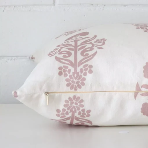 Pink patterned cushion cover laying sideways against brick wall. The square size and linen material are shown highlighting the seams.