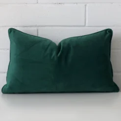 Bold rectangle emerald green cushion positioned in front of white brickwork. It is made from velvet fabric.