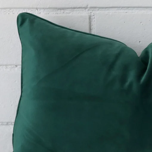 Rectangle cushion in emerald green colour sitting upright in front of a brick wall. It has been made from a quality velvet material.