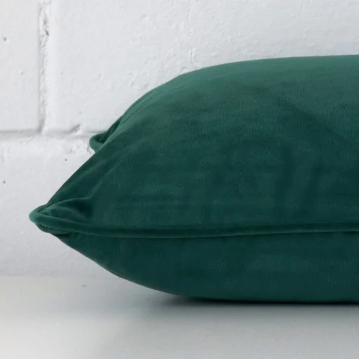 Side perspective showing seam of rectangle emerald green cushion cover that has velvet fabric.