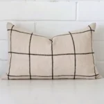 rectangle check cushion sitting upright in front of a brick wall. It has been made from a quality linen material.