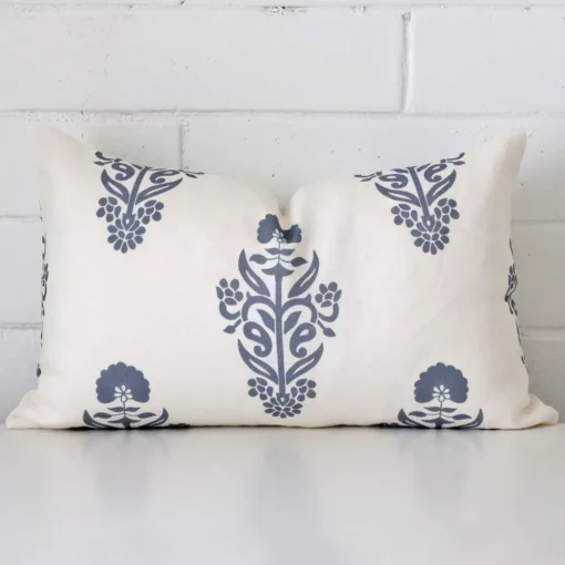 Linen rectangle cushion with a floral design in an upright position against a white brick wall. It is light blue in colour