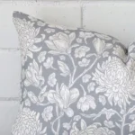 The corner of this light blue linen cushion is shown close up. The finer detail of its rectangle design and floral decorative finish can be seen.