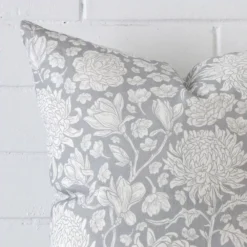 The corner of this light blue linen cushion is shown close up. The finer detail of its square design and floral decorative finish can be seen