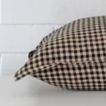 Gingham cushion cover laying sideways against brick wall. The square size and designer material are shown highlighting the seams.
