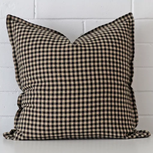 Designer square cushion with a gingham design in an upright position against a white brick wall.