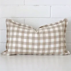 Gingham cushion cover sits against a white wall. It is constructed from a superior looking designer material and has rectangle dimensions.