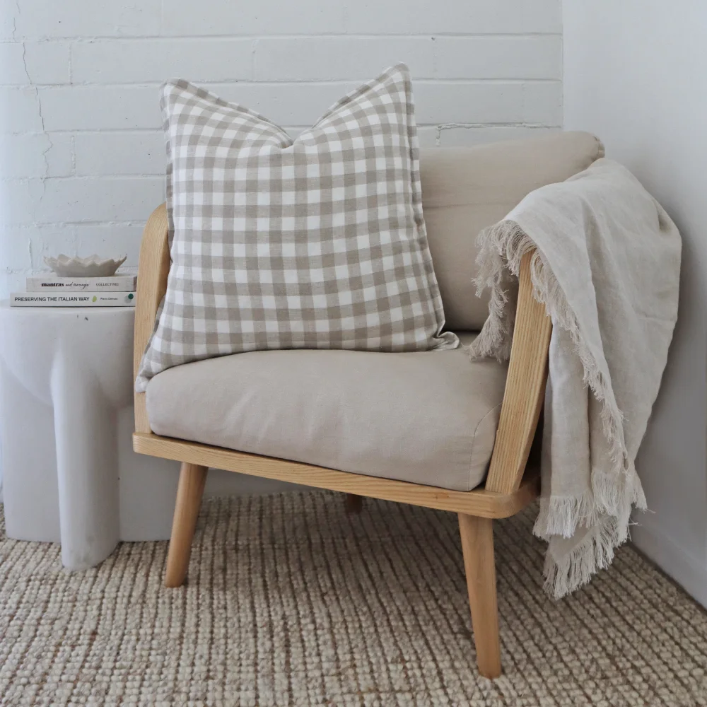 A gingham cushion is styled on a light coloured armchair with a throw.