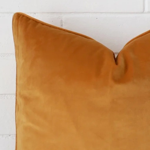 The corner of this gold mustard velvet cushion is shown close up. It has a square design.