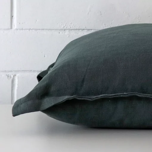 Green cushion laid horizontally. This perspective shows the edge of the linen fabric and its square shape.