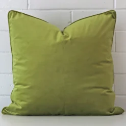 Green velvet cushion cover in front of a white wall. It has a square size and is made from a velvet material.