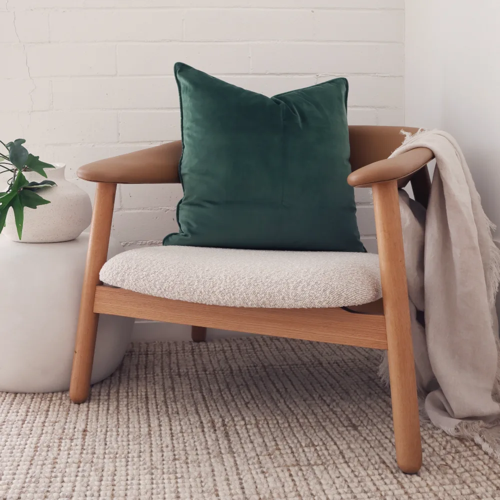 A green velvet cushion positioned on a curved armchair.