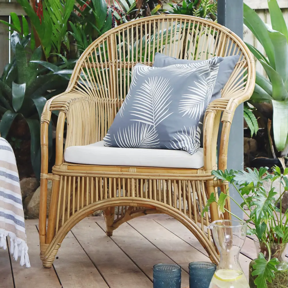 Two grey outdoor cushions layered on a rattan chair outside.