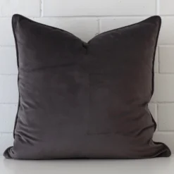 Bold square grey velvet cushion positioned in front of white brickwork.