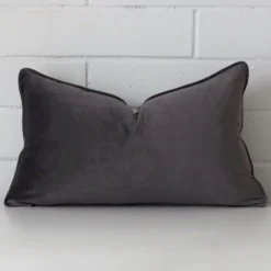Grey cushion cover sits against a white wall. It is constructed from a superior looking velvet material and has rectangle dimensions.