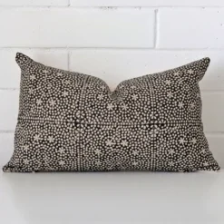 White wall with a cushion laying against it. It has a distinctive designer fabric and has a rectangle shape.