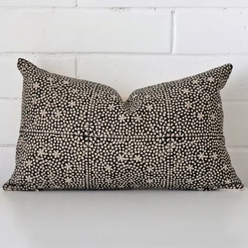 White wall with a cushion laying against it. It has a distinctive designer fabric and has a rectangle shape.