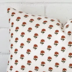 Rectangle floral cushion in terracotta colour sitting upright in front of a brick wall. It has been made from a quality linen material.
