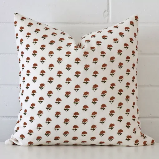 Terracotta floral cushion cover in front of a white wall. It has a square size and is made from a linen material.
