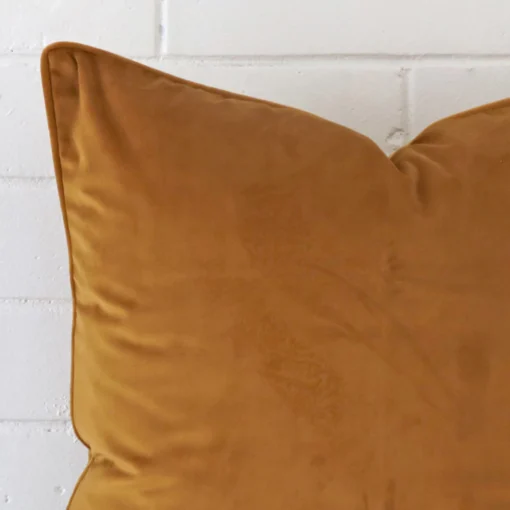 Cropped shot of top left corner of this honey mustard cushion cover. This viewpoint shows the velvet fabric and square shape with more precision.