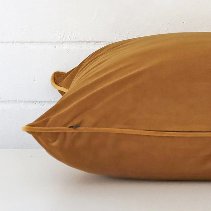 Velvet honey mustard cushion laying on its side. It has a square shape.