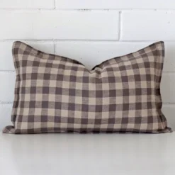 Designer rectangle cushion with a gingham design in an upright position against a white brick wall.