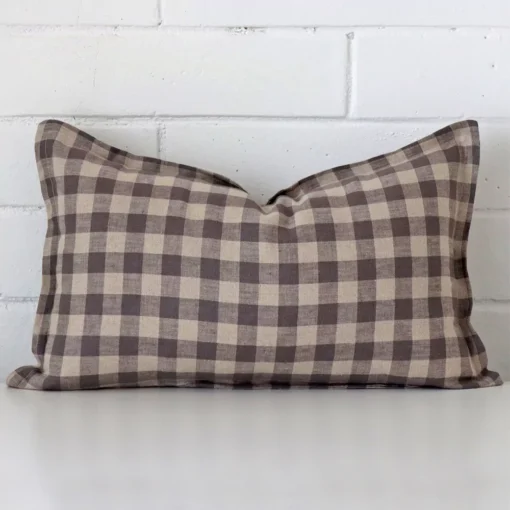 Designer rectangle cushion with a gingham design in an upright position against a white brick wall.