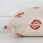 The edge of this linen rectangle cushion in rust is shown. The shot shows the floral design and the front and rear panels.