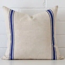 Bold square blue cushion positioned in front of white brickwork. Its striped style pops on the linen fabric.