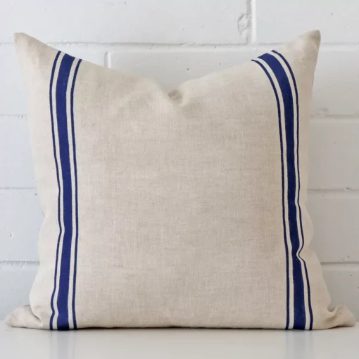 Bold square blue cushion positioned in front of white brickwork. Its striped style pops on the linen fabric.