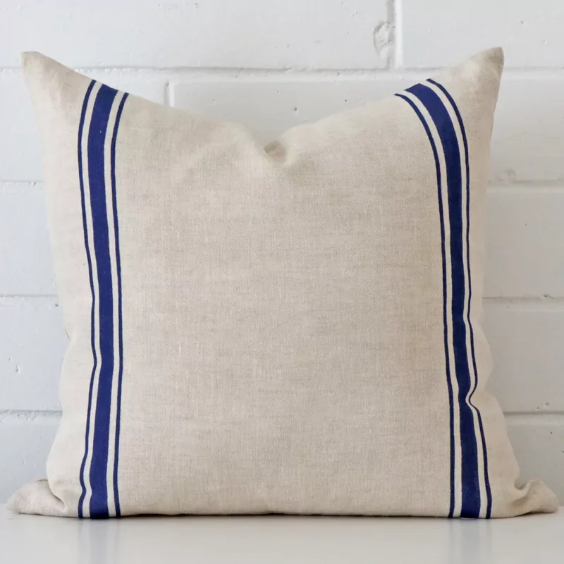 ivy-linen-blue-striped-cushion-cover-sc1005-45 Bold square blue cushion positioned in front of white brickwork. Its striped style pops on the linen fabric.