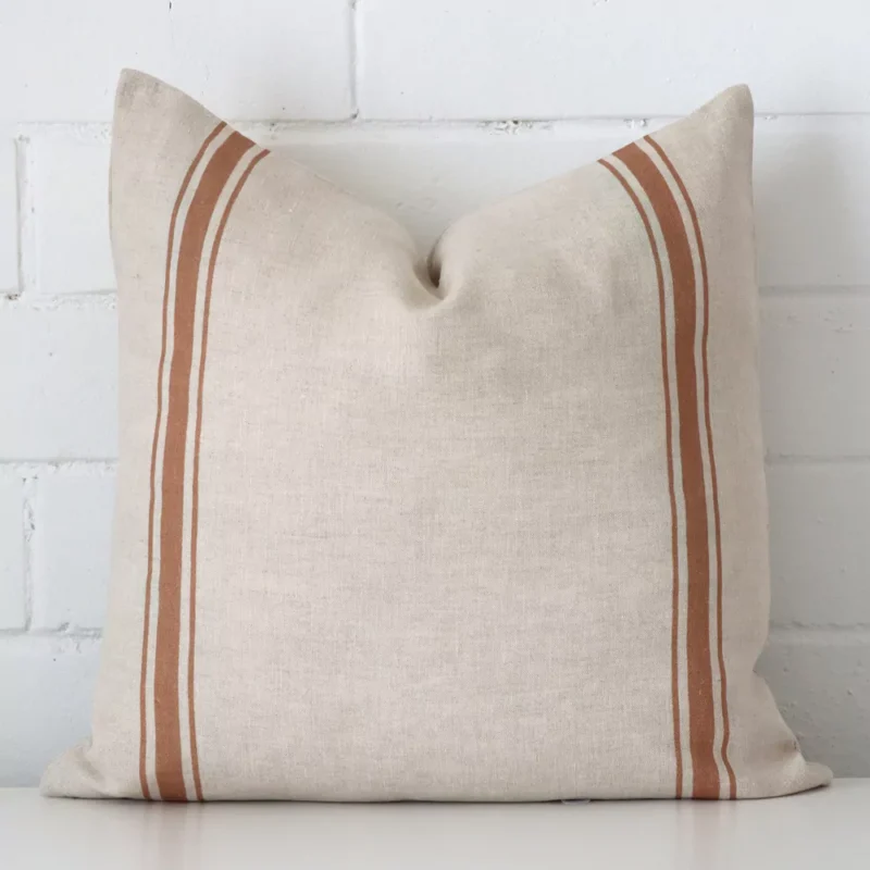 ivy-linen-terracotta-striped-cushion-cover-sc1004-45 An attractive striped linen cushion in front of a white brick wall. It has a square shape and is terracotta in colour.