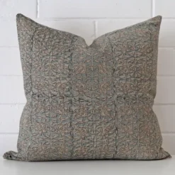 Floral cushion cover in front of a white wall. It has a square size and is made from a designer material.