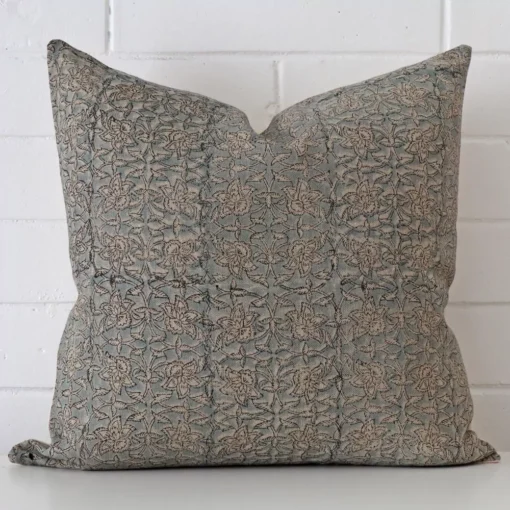 Floral cushion cover in front of a white wall. It has a square size and is made from a designer material.