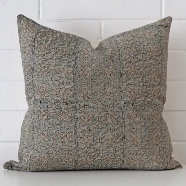 Floral cushion cover in front of a white wall. It has a square size and is made from a designer material.