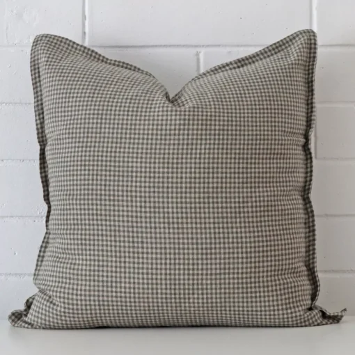 Bold square cushion positioned in front of white brickwork. Its gingham style pops on the designer fabric.