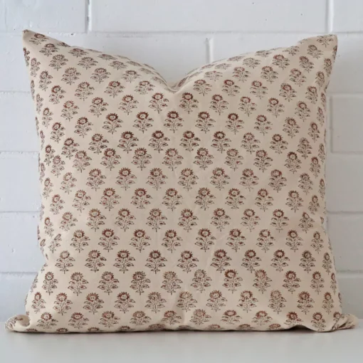 An attractive floral designer cushion in front of a white brick wall. It has a square shape.